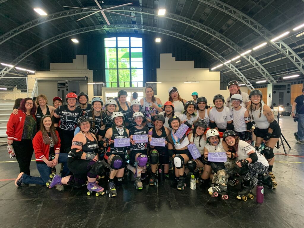 A group photo of BAD Comets in white jerseys and Monterey Bay Comets in purple jerseys. Several skaters hold up purple bandanas. 