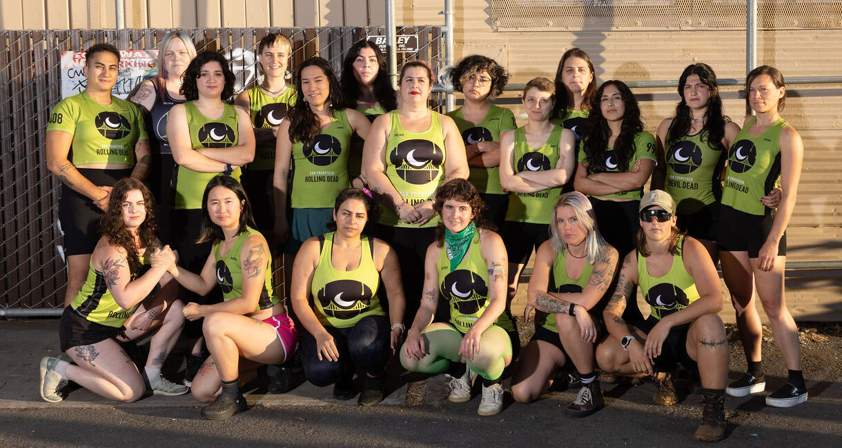 Group photo of San Francisco Rolling Dead players wearing green jerseys with the SF Rolling Dead logo of a white bridge with a white moon over a black circle. The players are standing in front of a corrugated metal wall